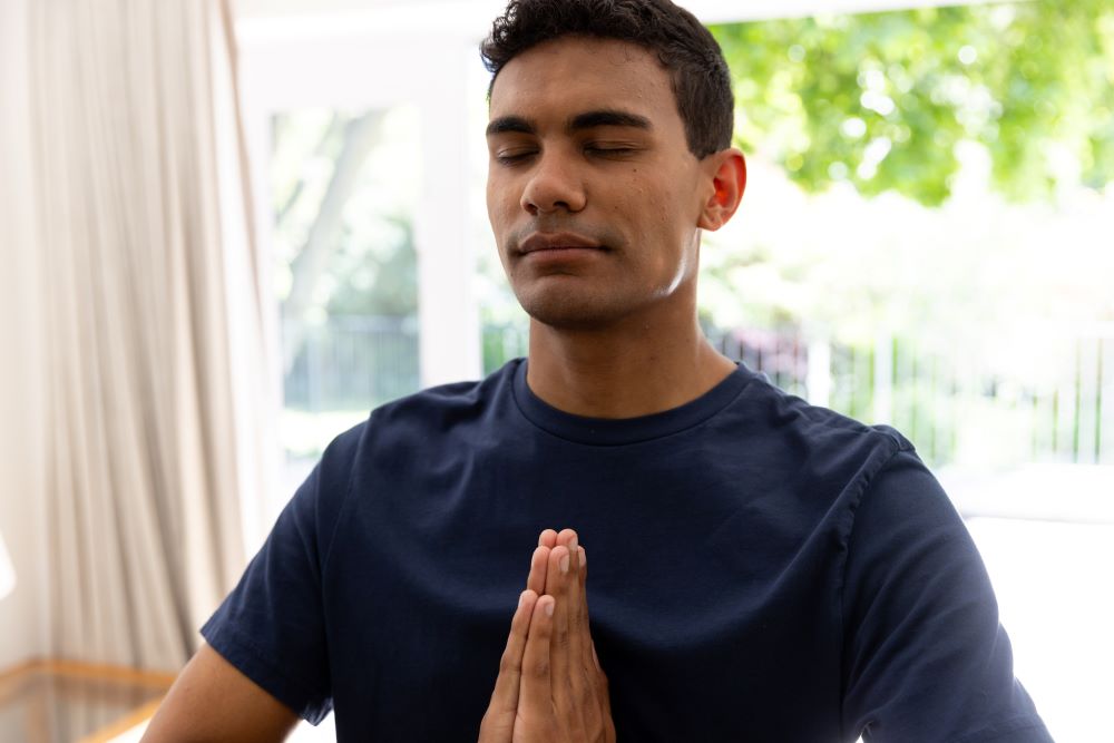 An attractive young man sits in a meditation pose with his eyes closed. Staying grounded: an antidote to our fast digital world.