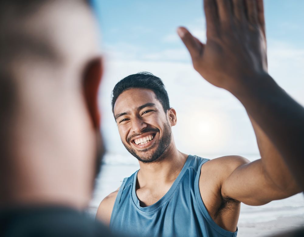 A young Asian man high-five's a friend and is enjoying the happy moment with a large smile. Staying grounded: an antidote to our fast digital world.