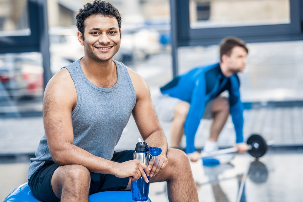 Young happy man sitting on a Swiss ball in workout gym. Pump Up Your Male Sexual Energy With Weight Training