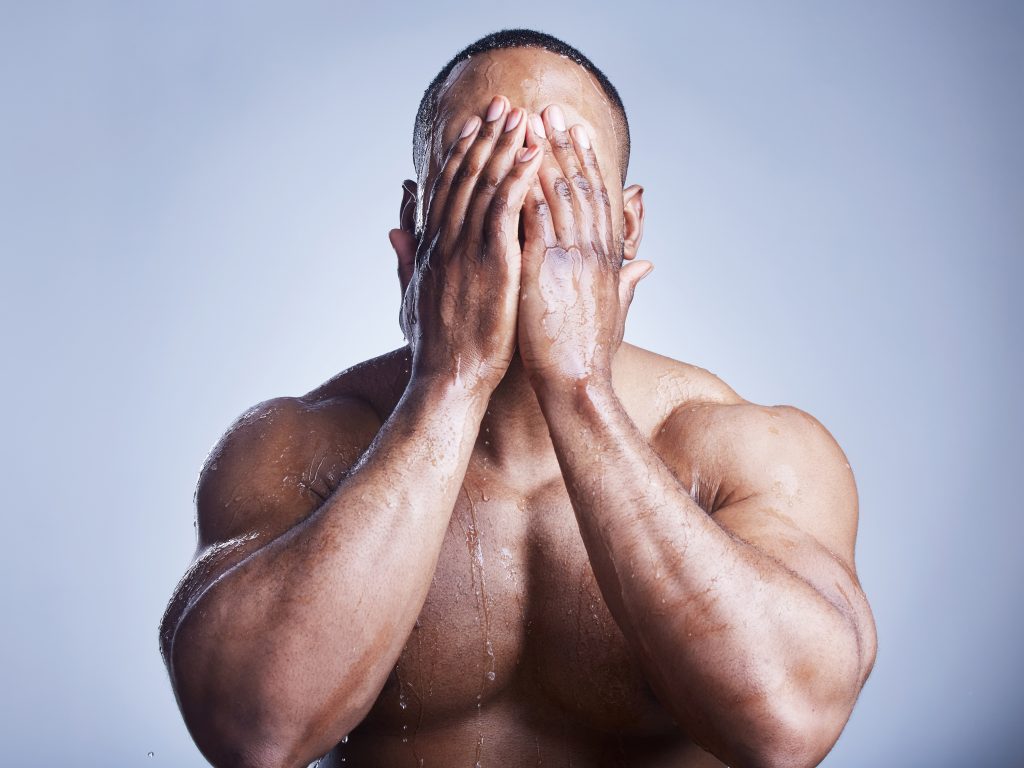 Black man with water dripping down his head and shoulders, hands covering his face depicting the concept of shame. Male Sexuality is Definitely Fluid: My Observations from 8 Years of Massage Practice.
