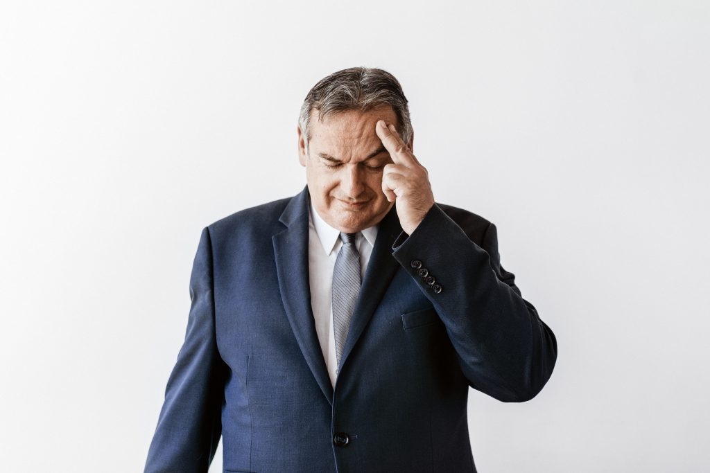 Older man in a suit with two fingers massaging forehead indicating facial expression of stress. Male Sexuality is Definitely Fluid: My Observations from 8 Years of Massage Practice.