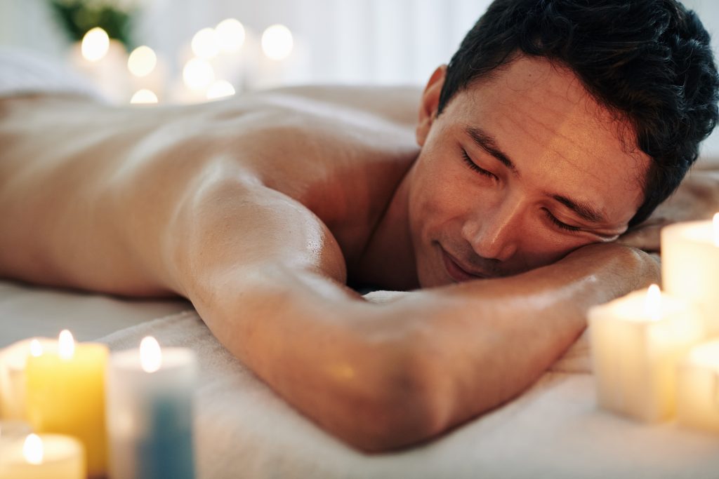 Happy and relaxed Asian man laying on a massage table. Deep Healing from the Transformative Power of Male Sensual Erotic Massage