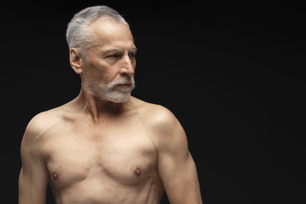 Portrait of serious gray haired, bearded, naked torso senior man looking away standing isolated on black background copy space. Behind the Scenes: What I Notice with Clients Seeking Male Erotic & Sensual Massage